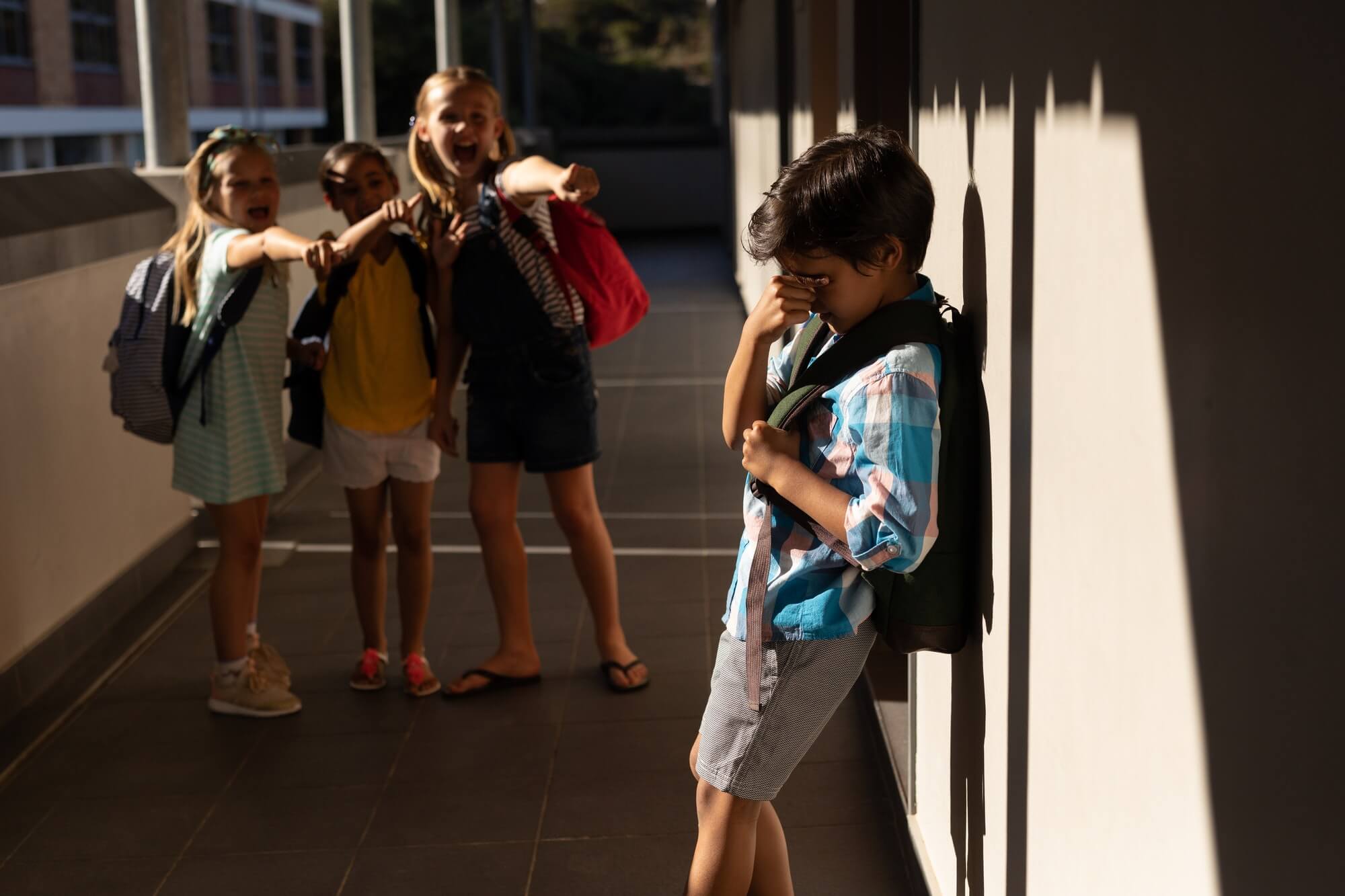Front view of school friends bullying a crying boy in hallway of elementary school